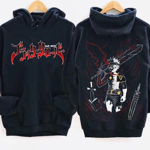 Może przedstawiać: Czarna bluza z kapturem z białym nadrukiem graficznym postaci z anime Black Clover. Na przodzie bluzy znajduje się napis "Black Clover".