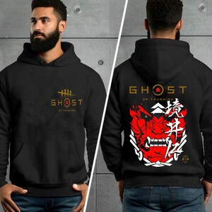 May include: Black hooded sweatshirt with a gold "Ghost of Tsushima" logo on the front and a red and white samurai mask with Japanese characters on the back.