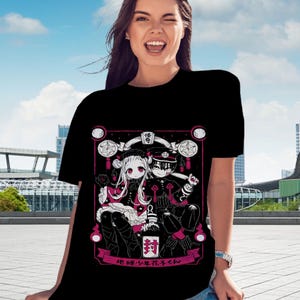 May include: Black t-shirt with a pink and white illustration of two anime characters. The characters are sitting on a throne with a pink background. The text "地縛少年花子くん" is written in pink below the characters.