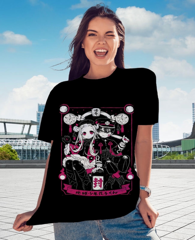 May include: Black t-shirt with a pink and white illustration of two anime characters. The characters are sitting on a throne with a pink background. The text "地縛少年花子くん" is written in pink below the characters.