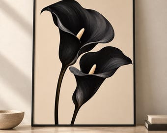 May include: A framed wall art print featuring two large black calla lily flowers with pale yellow spadices set against a solid light beige background. The artwork is enclosed in a thin black frame, showcasing a botanical illustration style.