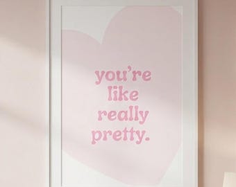 May include: A rectangular wall art print in a white frame featuring a large, pale pink heart shape on a white background. The text 'you're like really pretty.' is printed in the center in a soft pink, rounded, retro-style serif font.