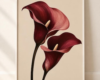 May include: A framed wall art print featuring two deep burgundy calla lilies with prominent cream-colored spadices. The flowers are set against a solid, neutral beige background, captured in a vertical orientation within a thin white frame.
