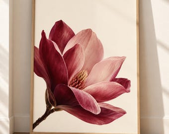 May include: A framed wall art print featuring a large, detailed illustration of a single magnolia flower. The flower has deep burgundy and soft pink petals with a textured yellow center, set against a solid cream background in a light wood frame.
