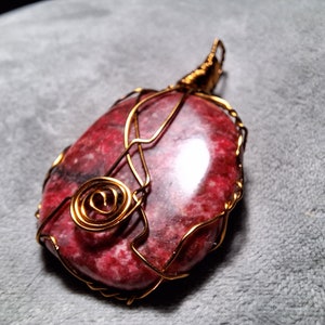 May include: A red and white gemstone pendant wrapped in gold wire. The wire is twisted into a spiral design.