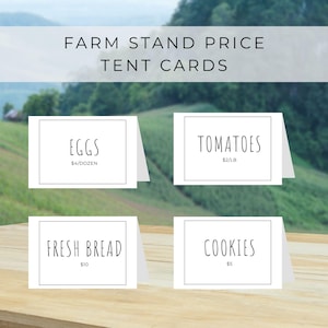 May include: White tent cards with black text, displaying "EGGS", "TOMATOES", "FRESH BREAD", and "COOKIES". The cards are on a wooden surface with a blurred green and blue background. The top text reads "FARM STAND PRICE TENT CARDS".