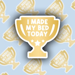 May include: Gold trophy sticker with the text "I made my bed today" in white. The sticker is on a light blue background with a pattern of smaller gold trophy stickers.