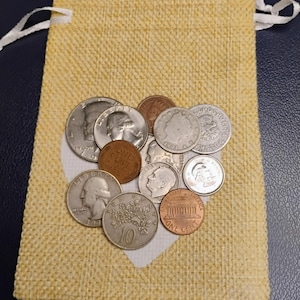 May include: A yellow burlap pouch with a white heart-shaped cutout, filled with various coins. The coins include a half dollar, a quarter, a dime, a penny, and other currency. The pouch has a drawstring closure.