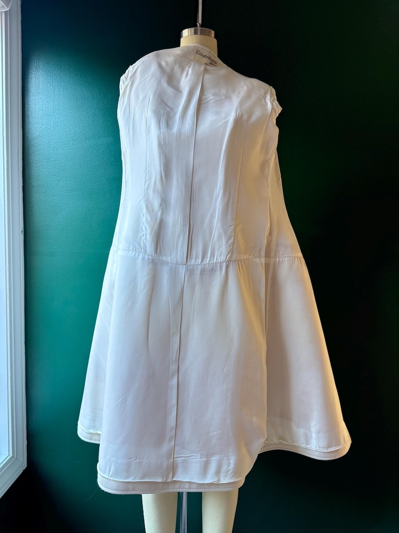 May include: A white satin slip with a gathered skirt and a label that reads "Courreges Paris".