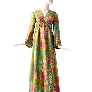 May include: A long, flowing green, yellow, pink, and blue floral print dress with a jeweled belt. The dress has long sleeves with bell bottoms and a V-neck.
