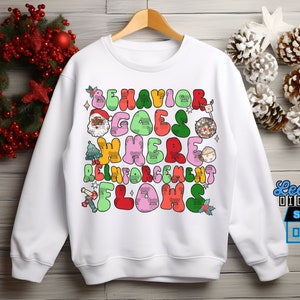 May include: White sweatshirt featuring a colourful graphic design that reads "Behaviour Goes Where Reinforcement Flows". The graphic includes a Santa Claus, a Christmas tree, a globe, and other festive elements.