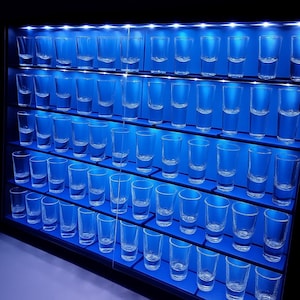Könnte beinhalten: Eine blau beleuchtete Vitrine mit Reihen von klaren Schnapsgläsern. Der Schrank hat mehrere Regale, die jeweils mehrere Gläser halten. Die Beleuchtung erzeugt einen auffälligen visuellen Effekt, ideal für eine Sammlung.