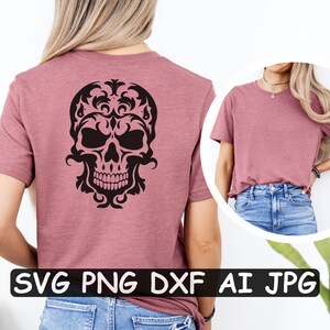 K&ouml;nnte beinhalten: Ein pinkfarbenes T-Shirt mit einem schwarzen Totenkopf-Design auf der R&uuml;ckseite. Der Totenkopf ist von komplizierten floralen Mustern umgeben. Der Text "SVG PNG DXF AI JPG" ist unten im Bild gedruckt.