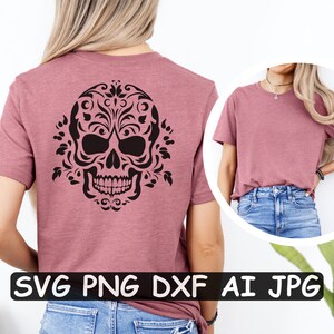 Może przedstawiać: R&oacute;żowy t-shirt z czarnym kwiatowym wzorem czaszki z tyłu. Wz&oacute;r zawiera skomplikowane detale i stylizowaną czaszkę z elementami kwiatowymi. Koszulka jest pokazana na modelce w niebieskich dżinsach.