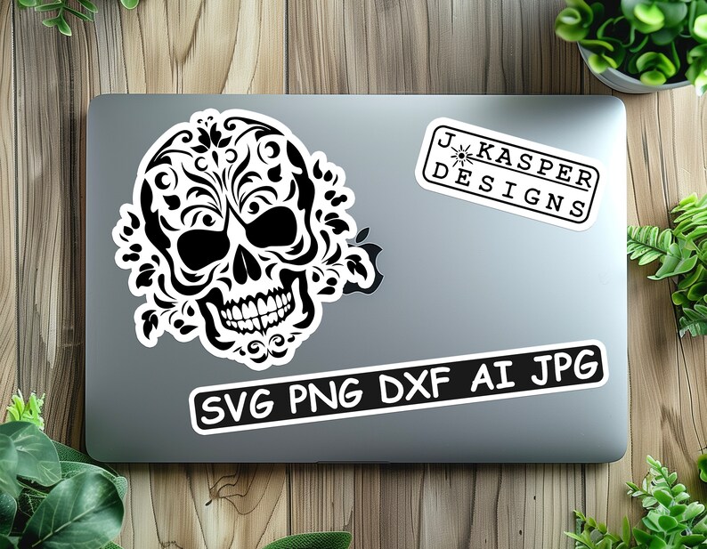 Może przedstawiać: Czarno-biała czaszka z kwiatowymi wzorami, na srebrnym laptopie z białą naklejką z napisem "SVG PNG DXF AI JPG" i inną białą naklejką z napisem "J. Kasper Designs".