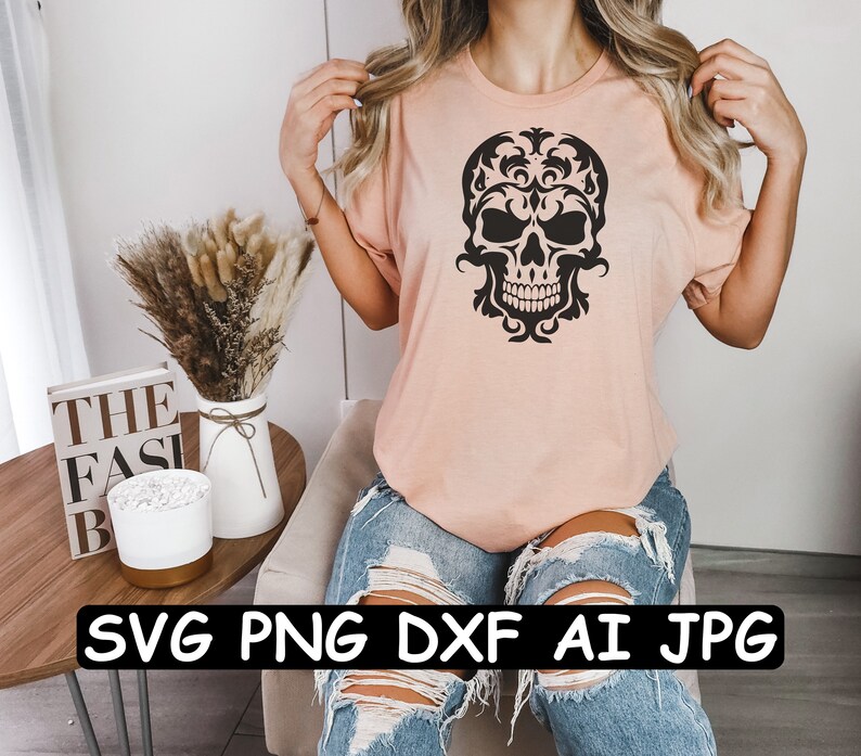 K&ouml;nnte beinhalten: Ein pinkfarbenes T-Shirt mit einem schwarzen floralen Totenkopf-Design. Das Shirt wird von einer Person mit langen blonden Haaren getragen. Der Text "SVG PNG DXF AI JPG" ist auf einer Oberfl&auml;che vor der Person gedruckt.