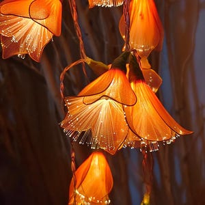 May include: A decorative string of orange flower lights. Each flower has a translucent petal structure with a glowing centre. The lights are strung on thin, copper-coloured wires, creating a warm ambiance. Suitable for home decor and special events.
