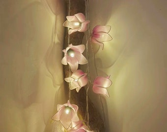 May include: A string of pink flower-shaped fairy lights. The lights are arranged along a brown branch, with each flower illuminated by a small bulb. The flowers are a soft pink color, creating a warm and inviting glow. The lights are ideal for home decor.