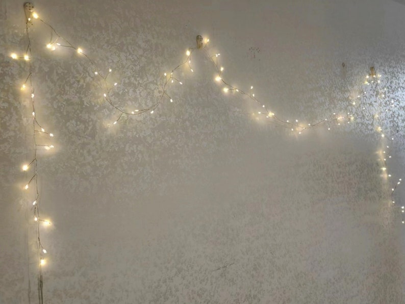 Pu&ograve; includere: Una ghirlanda di luci bianche a forma di arco, appesa a un muro bianco. Le luci creano un'atmosfera festosa e fantasiosa.