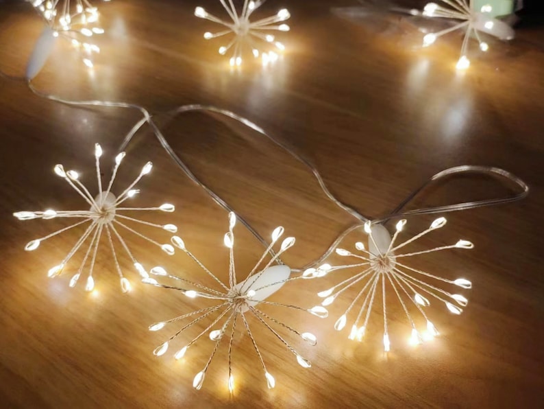 K&ouml;nnte beinhalten: Eine Lichterkette mit wei&szlig;en Lichterketten im Sternburst-Design. Die Lichter sind mit einem klaren Draht verbunden und werden von einem Batteriepack betrieben. Die Lichter sind perfekt, um jedem Raum einen Hauch von Magie zu verleihen.