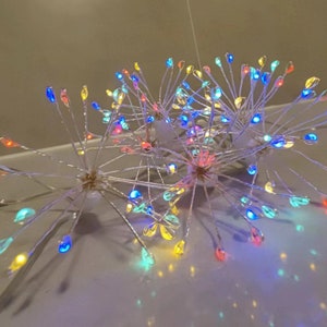K&ouml;nnte beinhalten: Ein Satz mit drei mehrfarbigen LED-Lichterketten in Form einer Feuerwerksfont&auml;ne. Die Lichter sind auf einem klaren Draht aufgef&auml;delt und haben verschiedene Farben, darunter Rot, Blau, Gr&uuml;n, Gelb und Wei&szlig;.