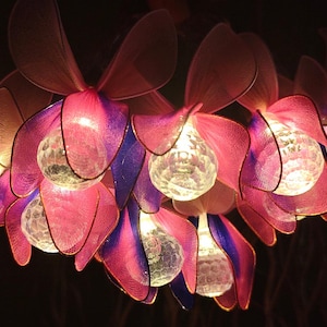 May include: A decorative chandelier with a floral design. The petals are pink and purple, and each flower holds a clear, spherical light. The chandelier emits a warm glow, suitable for home decor.