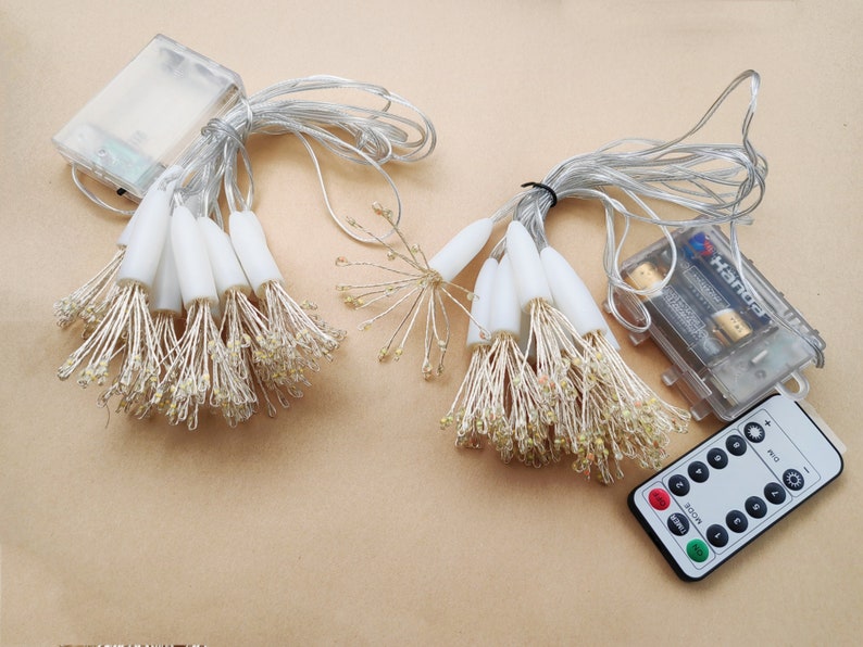K&ouml;nnte beinhalten: Ein Satz wei&szlig;er Lichterketten mit einer Fernbedienung. Die Lichter sind batteriebetrieben und haben einen warmwei&szlig;en Schein. Die Fernbedienung hat Kn&ouml;pfe f&uuml;r Ein/Aus, Timer und verschiedene Lichtmodi.
