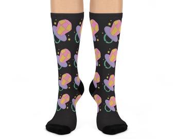 Puede incluir: Calcetines negros hasta la rodilla con un patrón repetido de diseños de chupetes. Los chupetes tienen un esquema de color rosa, amarillo y morado, con pequeñas estrellas amarillas esparcidas sobre el fondo negro. Los calcetines se llevan en las piernas de una persona.