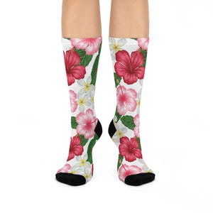Può includere: Un paio di calzini bianchi con un vivace motivo floreale. Il design presenta fiori di ibisco rossi e rosa, fiori di frangipani bianchi e foglie verdi. I calzini hanno talloni e dita neri.