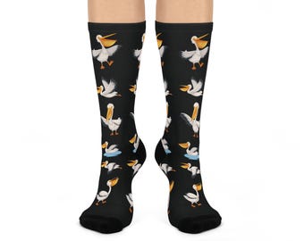 May include: Black socks featuring a repeating pattern of white and yellow pelican illustrations. The pelicans are depicted in various poses, some in flight and others swimming. The socks have black toes and heels, and the pelicans are set against a black background.