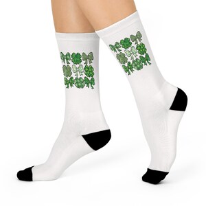 Puede incluir: Calcetines blancos con talones y puntas negros, decorados con tréboles y lazos verdes. Los calcetines son hasta la rodilla y tienen un tema del Día de San Patricio.