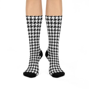 May include: A pair of knee-high socks with a black and white houndstooth pattern. The socks have black heels and toes. The socks are displayed against a white background.