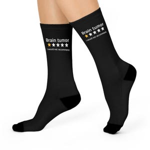 Può includere: Calzini neri con la scritta "Brain tumor" e una valutazione a una stella, con la frase "I would not recommend." I calzini sono indossati sulle gambe di una persona.