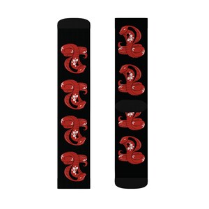 Könnte beinhalten: Ein Paar schwarze Socken mit einem roten Schlangenmuster. Die Schlangen sind zusammengerollt und haben eine weiße Blume im Maul. Die Socken sind eine lustige und stilvolle Möglichkeit, jedem Outfit eine persönliche Note zu verleihen.