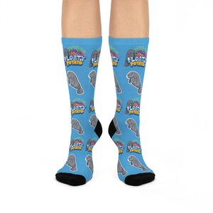 May include: A pair of blue socks with a repeating pattern of gray manatees and the words "FLOATY POTATO" in a colorful design. The socks have black heels and toes.