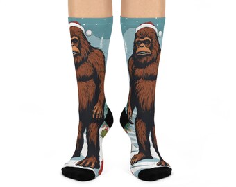 May include: A pair of black socks with a wintery scene featuring a Bigfoot wearing a Santa hat. The socks are blue and white with a snowy background.