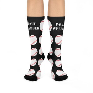 Könnte beinhalten: Schwarze Kniestrümpfe mit einem Muster aus weißen Basebällen mit roten Nähten. Der Text "PAUL WEBBER" ist weiß auf der Oberseite jeder Socke aufgedruckt.
