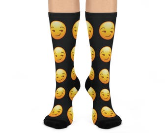 May include: Black knee-high socks featuring a repeating pattern of yellow emoji faces with a sly grin. The socks are made of a soft material and are designed to fit comfortably. The socks are a fun and playful accessory.
