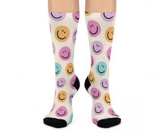 May include: A pair of white socks with a colorful smiley face pattern. The socks are cream colored with pink, yellow, and blue smiley faces.