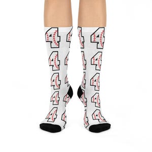 Könnte beinhalten: Weiße Socken mit einem sich wiederholenden Muster der Zahl 4, die wie ein Baseball gestaltet ist. Die Zahl ist schwarz mit roten Nähten.