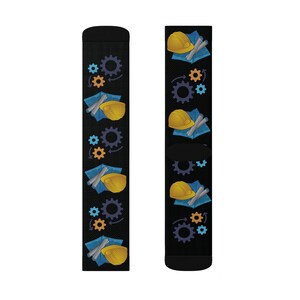 May include: Black socks with a repeating pattern of yellow construction hats, blueprints, and gears in shades of blue, orange, and purple. The socks are designed for construction workers or those in related fields.