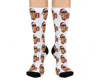 May include: White socks featuring a repeating pattern of a cartoon hot dog wearing sunglasses and a Santa hat, holding a wrapped gift. The socks have black heels and toes.