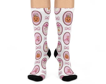 May include: White socks with a repeating pattern of Halloween-themed illustrations. The design includes pumpkins, ghosts, cowboy boots, and bows, all framed in pink oval medallions. The socks have black heels and toes.