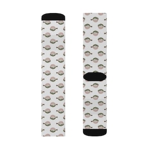 May include: A pair of socks with a repeating pattern of a light pink circle with a green design on a white background. The socks have black heels and toes.