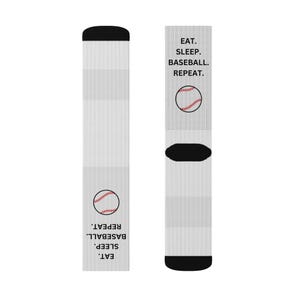 Könnte beinhalten: Ein Paar weiße Socken mit schwarzen Akzenten. Jede Socke zeigt eine Baseball-Grafik und den Text "EAT. SLEEP. BASEBALL. REPEAT." in Schwarz. Die Socken haben eine gerippte Textur.