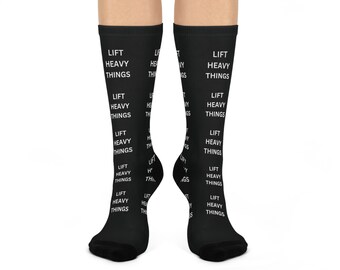 May include: Black socks with the words "LIFT HEAVY THINGS" printed in white. The text is repeated multiple times down the length of the socks. The socks are visible from the knees down.