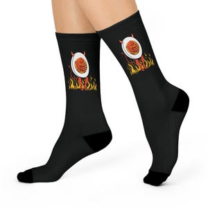 Peut inclure: Chaussettes noires avec un motif de diable de dessin animé tenant une assiette de spaghettis et de boulettes de viande. Le diable est représenté dans les flammes. Les chaussettes ont des talons et des orteils noirs.