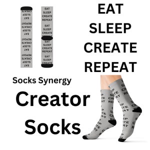 May include: Gray socks with the words "EAT SLEEP CREATE REPEAT" printed repeatedly. The socks are displayed on a person's legs, with the words also printed on the socks. The words "Socks Synergy" and "Creator Socks" are also visible.