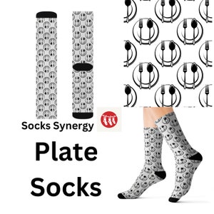 May include: Gray socks with a repeating pattern of smiling faces and cutlery. The socks have black heels and toes. The words "Plate Socks" are printed in large black letters.