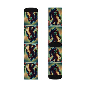 May include: A pair of black socks featuring a repeating pattern of a Bigfoot-like creature wearing a green bow. The background includes Christmas trees and wrapped gifts. The socks are designed for a comfortable fit.